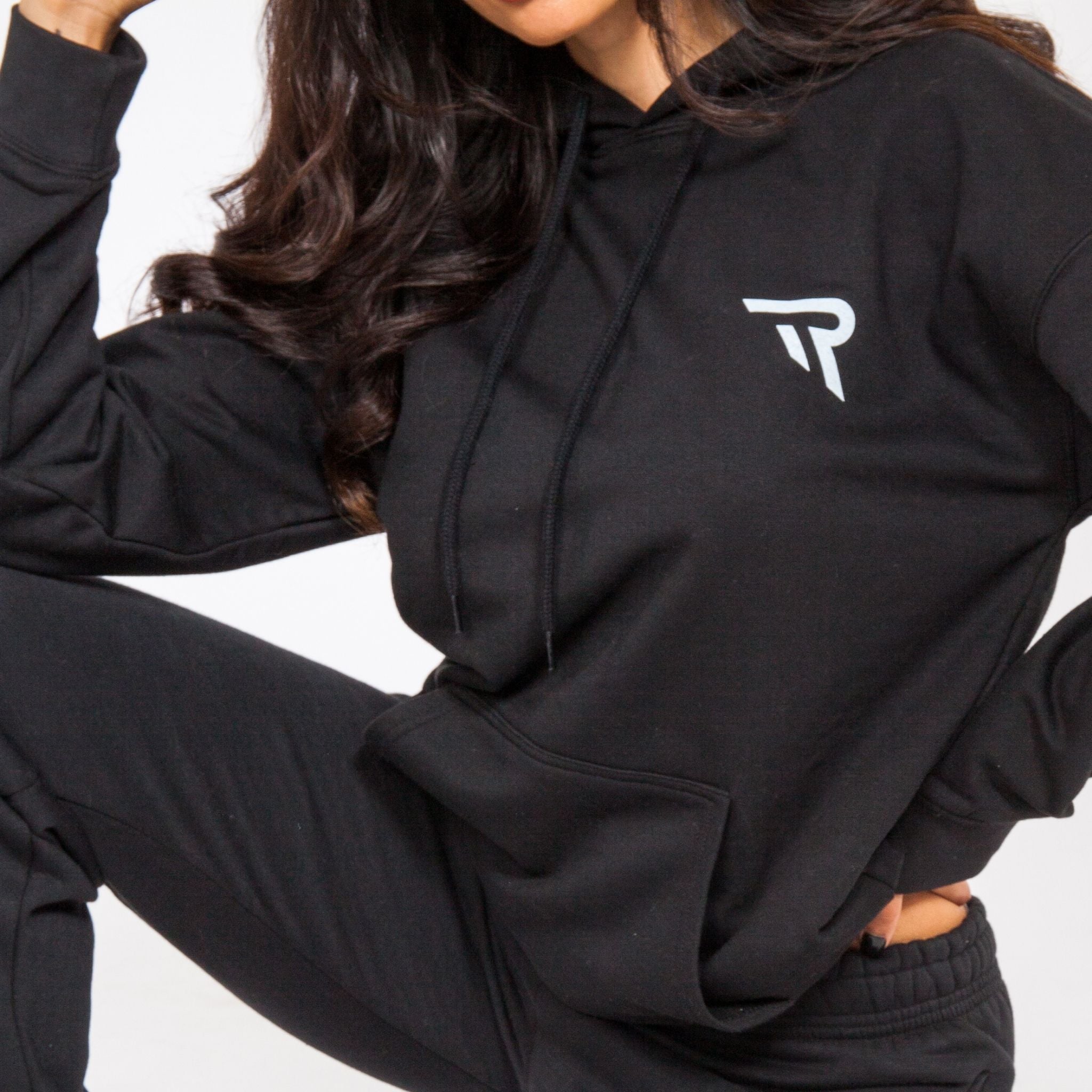 Close up of Female posing black oversized hoodie in studio with a zoom into logo for Re Tech UK and kangaroo pouch